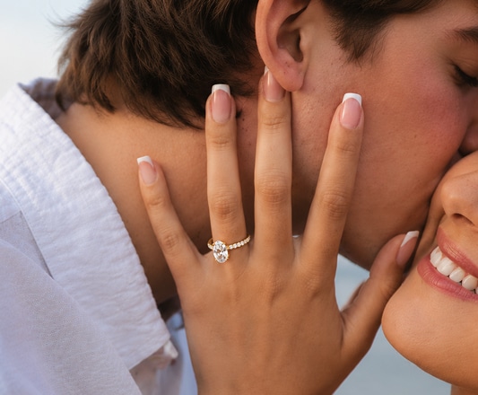 Smiling woman embracing her partner while wearing a yellow gold oval-cut lab-created diamond engagement ring.