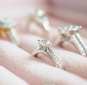 Close up of multiple sparkling lab-grown diamond rings safely secured in the soft, fabric-lined slots of a pink velvet jewelry box.