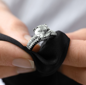Hands safely holding a white gold round-cut lab-grown diamond engagement ring with a black fabric pouch to prevent micro-abrasions.