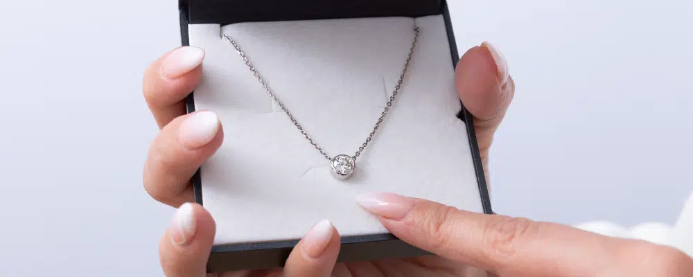 Elegant round diamond bezel set necklace draped over a purple silk ribbon, highlighting the sleek profile of bezel vs prong settings for a buying guide