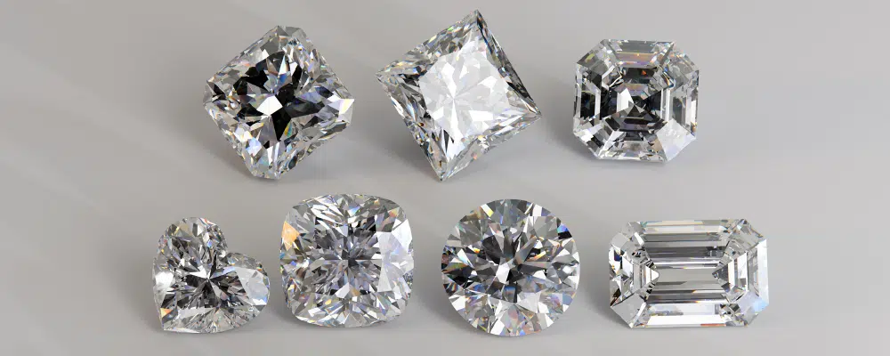 An array of loose diamonds displaying various geometric cuts including emerald, round brilliant, radiant, heart, cushion, princess, and asscher shapes.