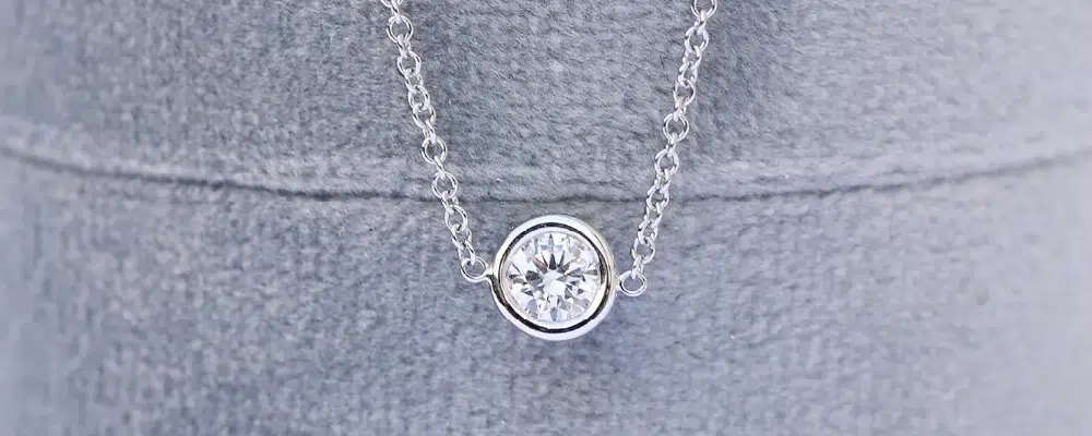 Unique modern half-bezel solitaire diamond necklace on a dark surface, showcasing an alternative to traditional prong and full bezel sets