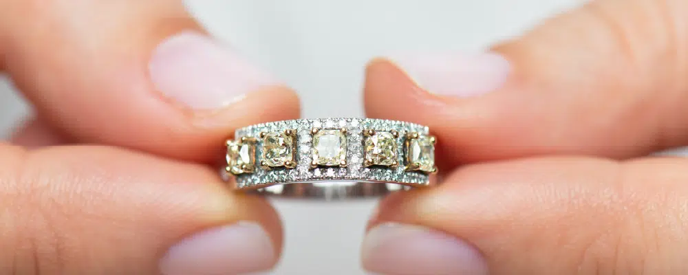 A luxury fancy yellow diamond 5-stone ring featuring cushion cut stones in a thick diamond pavé band