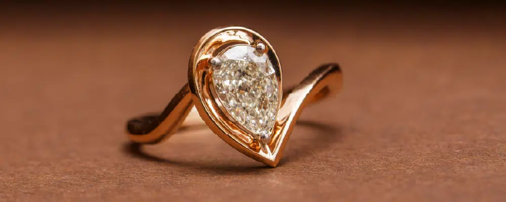 Unique bezel set pear shaped diamond ring with a modern V-shaped gold split shank band.