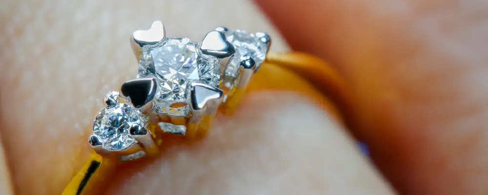 Close up of a gold three stone diamond ring with unique heart shaped prongs symbolizing love in the past present and future.