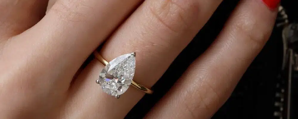 1.5 carat pear shaped diamond solitaire engagement ring on a gold band showing finger coverage and scale.