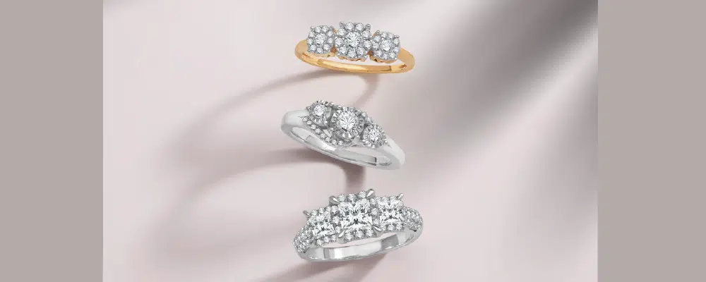 Collection of three stone engagement rings in yellow gold and white gold featuring round and princess cut diamond clusters.