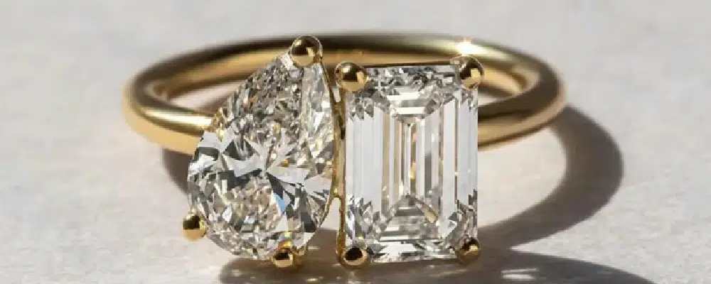 Toi et Moi engagement ring featuring a pear shaped diamond and emerald cut diamond in a yellow gold two-stone setting.