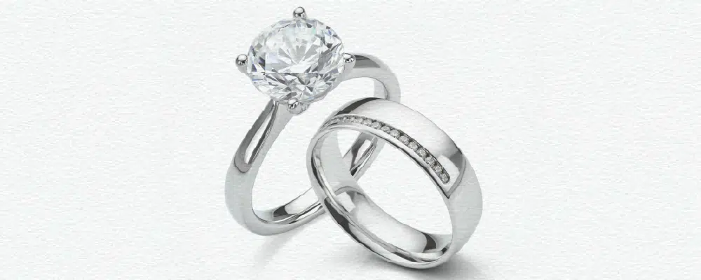 Modern pairing of a classic round white gold solitaire engagement ring with a wide, channel-set diamond wedding band
