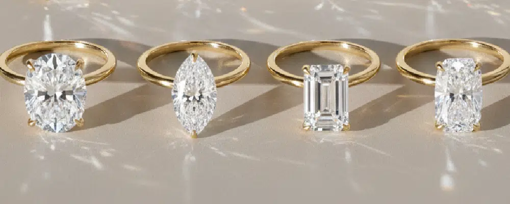 Row of 3 carat gold solitaire rings featuring oval, marquise, emerald, and elongated cushion cut diamonds.