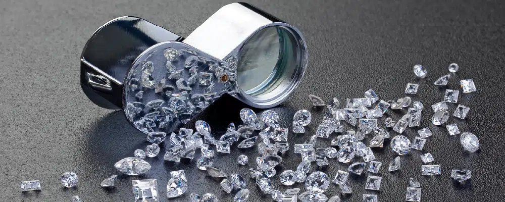 A jeweler's loupe surrounded by various loose diamonds on a dark surface, representing the process of making the perfect diamond choice.