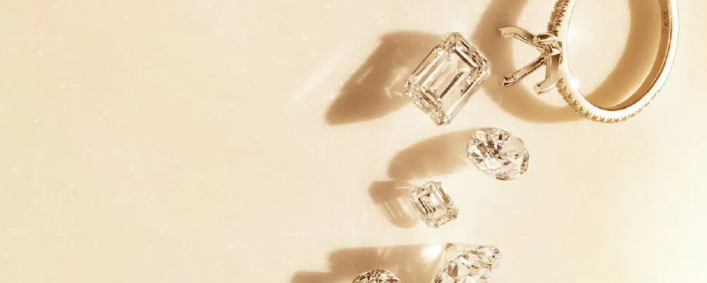 Top-down view of loose emerald and round cut diamonds next to a pave-set engagement ring band, illustrating diamond shape choices for solitaire rings.