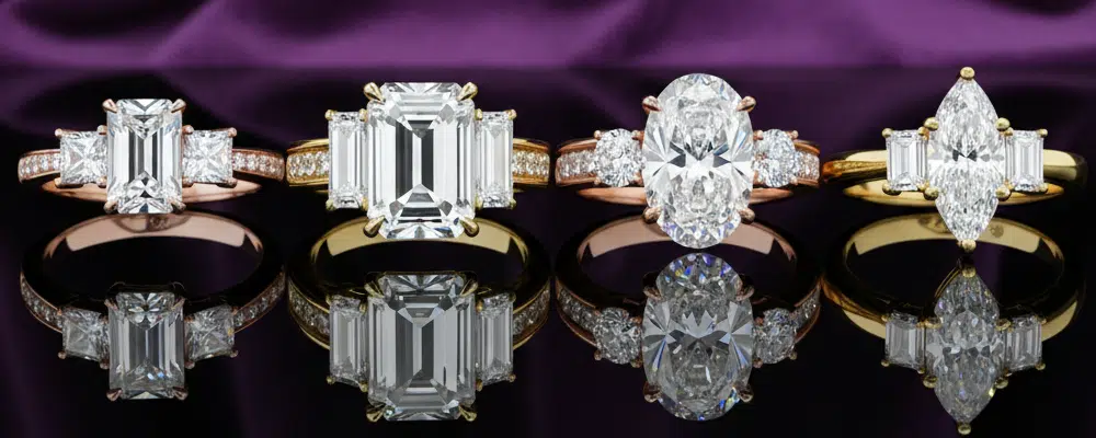 Four different multi-stone diamond engagement ring designs including emerald cut baguette side stones and oval cuts reflected on a black surface