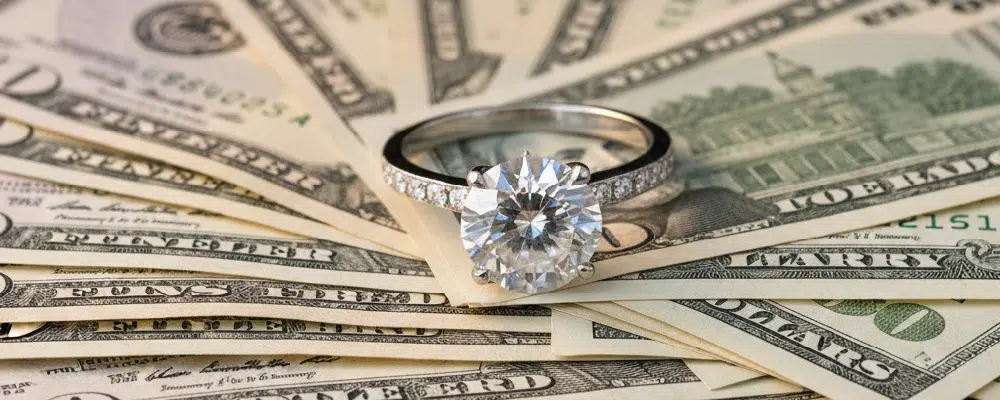 Round brilliant solitaire diamond engagement ring on cash representing average engagement ring costs and jeweler budgeting tips.