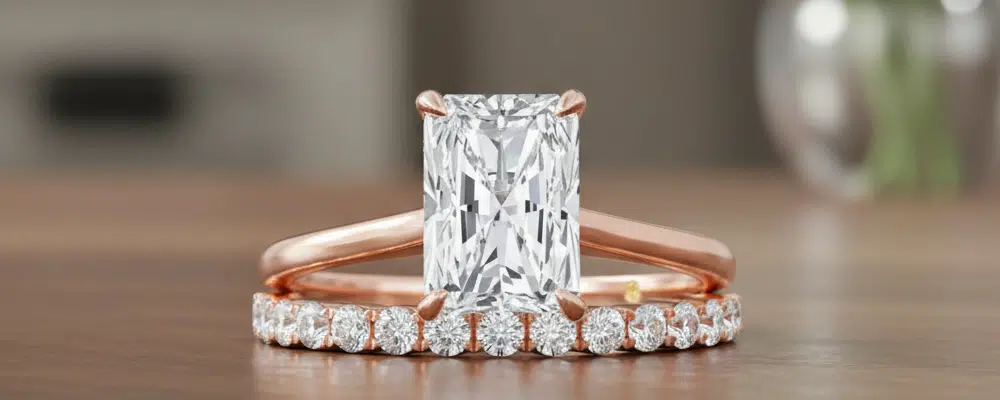 Rose gold radiant cut engagement ring paired with a pave diamond wedding band set on a wooden surface.