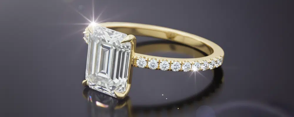 A yellow gold emerald cut ring with a delicate diamond micro-pavé band showcasing a distinct step-cut sparkle