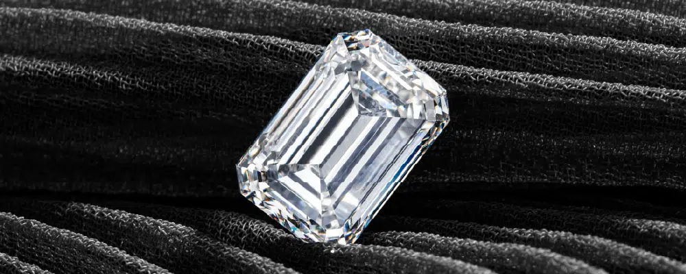 An unmounted loose emerald cut diamond displaying clean parallel facets on a black pleated texture