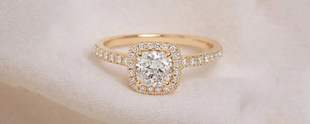 A delicate yellow gold cushion cut halo engagement ring featuring a slim pavé diamond band.