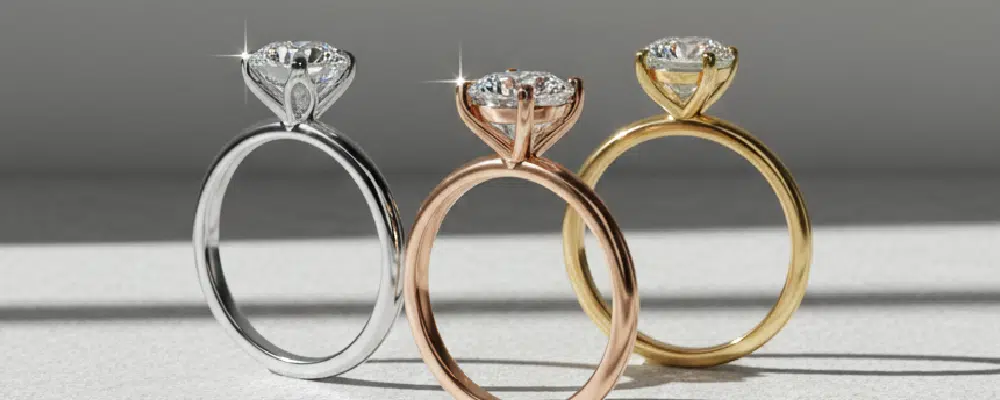 Side by side view of three classic solitaire engagement rings in white gold rose gold and yellow gold on a stone surface