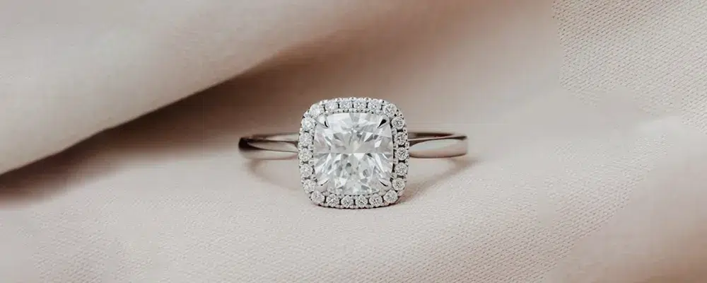 Cushion cut halo engagement ring with a polished plain platinum band on soft fabric.