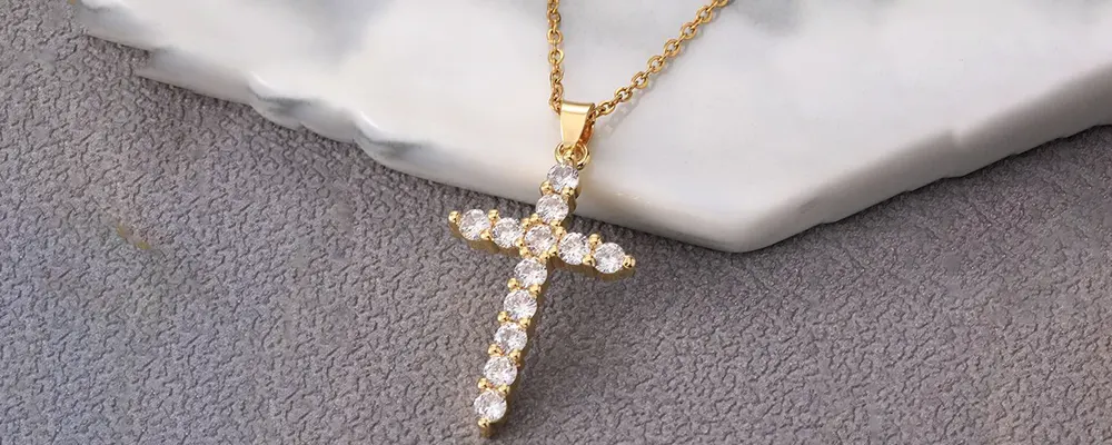 Dainty diamond cross pendant in a shared prong yellow gold setting on white marble.