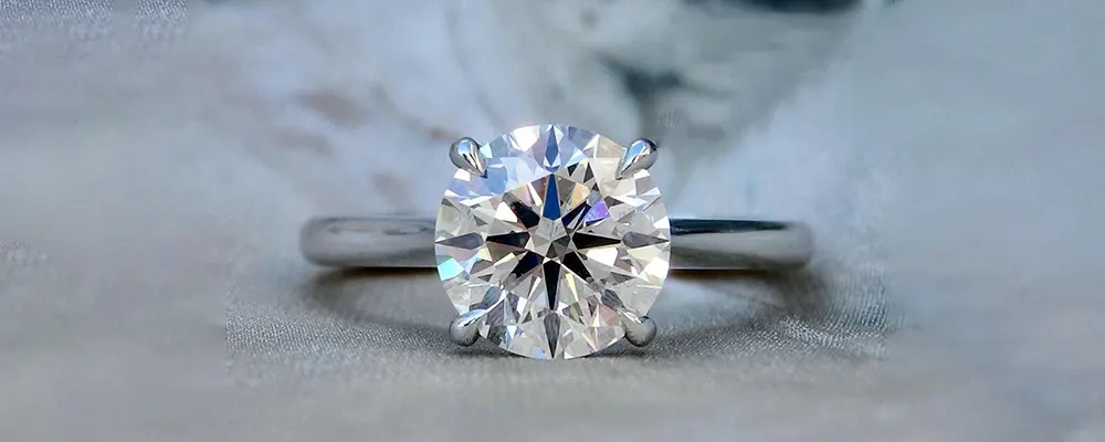 A classic round brilliant solitaire engagement ring featuring a custom white gold 4 prong setting on a silk fabric background