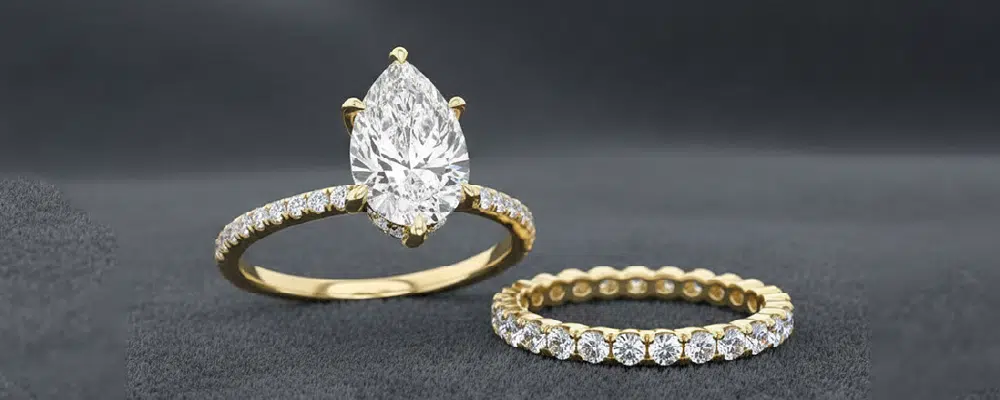 A classic pear cut diamond engagement ring on a yellow gold pavé band displayed next to a matching yellow gold diamond eternity wedding band