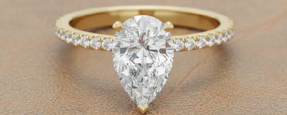 A classic pear shaped diamond solitaire ring on a 14k yellow gold pavé band showcasing an alternative to a hidden halo pear ring design