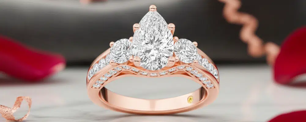 A romantic rose gold three stone pear engagement ring style featuring brilliant side diamonds and a pavé band