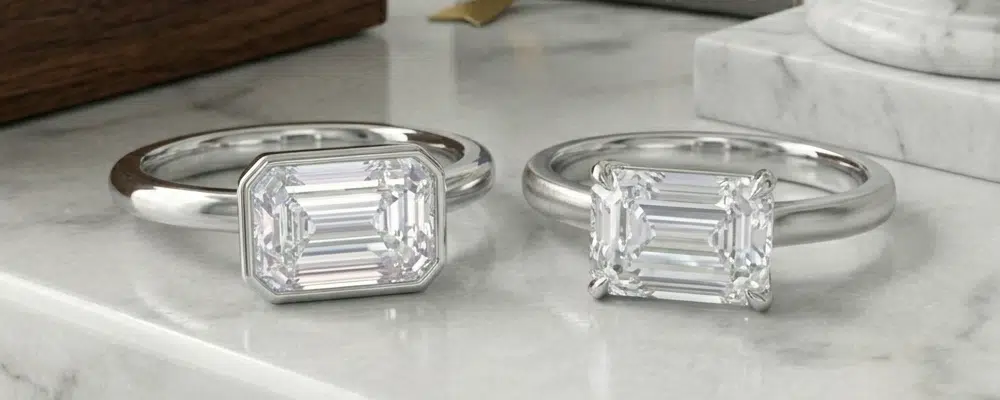 Comparison of a modern bezel set and a classic prong set east-west emerald cut engagement ring in platinum