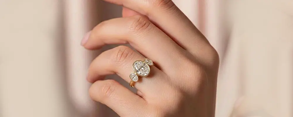 On-hand view of a secure luxury three stone oval diamond engagement ring with a full bezel setting.