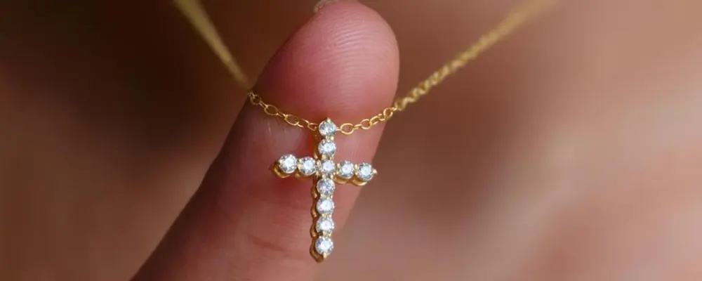 Close up view of a small dainty diamond cross pendant on a delicate yellow gold chain.