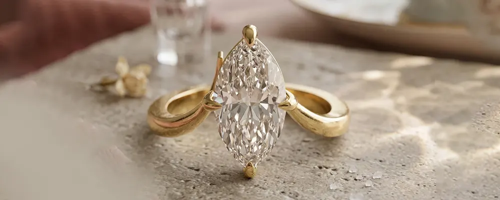 A unique marquise cut diamond engagement ring featuring a modern split shank yellow gold band resting on a textured stone surface.