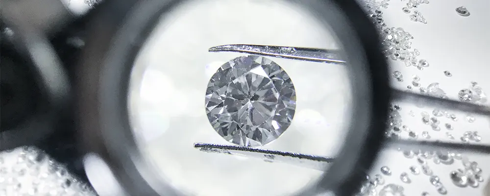 A close-up view through a jeweler's loupe of a round diamond held in tweezers, showcasing custom diamond selection for unique engagement rings