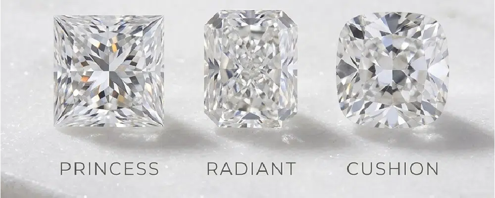 A comparison of loose princess radiant and cushion cut diamonds side by side on a marble surface highlighting unique shape differences for halo settings