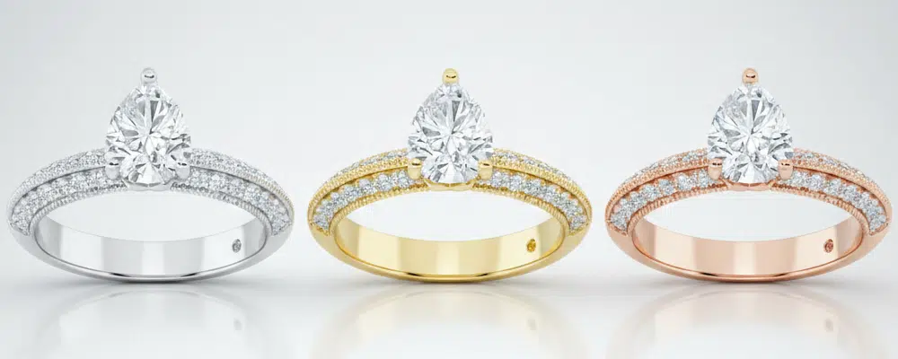 Three pear shaped diamond engagement rings compared side by side in platinum yellow gold and rose gold vintage milgrain bands