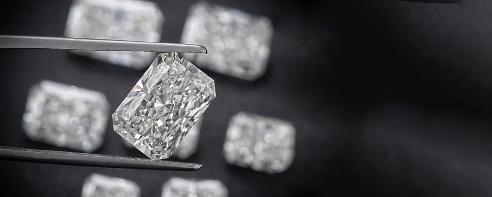A professional jeweler using tweezers to inspect a loose radiant cut lab diamond for clarity and optical perfection over a selection of loose gems.