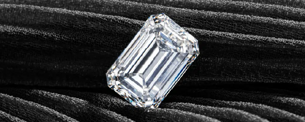 A loose emerald cut diamond showing clean step cuts and parallel facets on black fabric before horizontal orientation setting