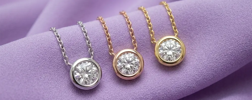 Three round bezel set diamond pendant necklaces in white gold rose gold and yellow gold on purple fabric.