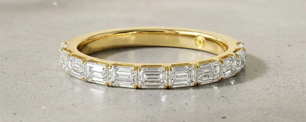 An emerald cut diamond eternity wedding band set in yellow gold, showcasing a modern east-west horizontal diamond orientation.