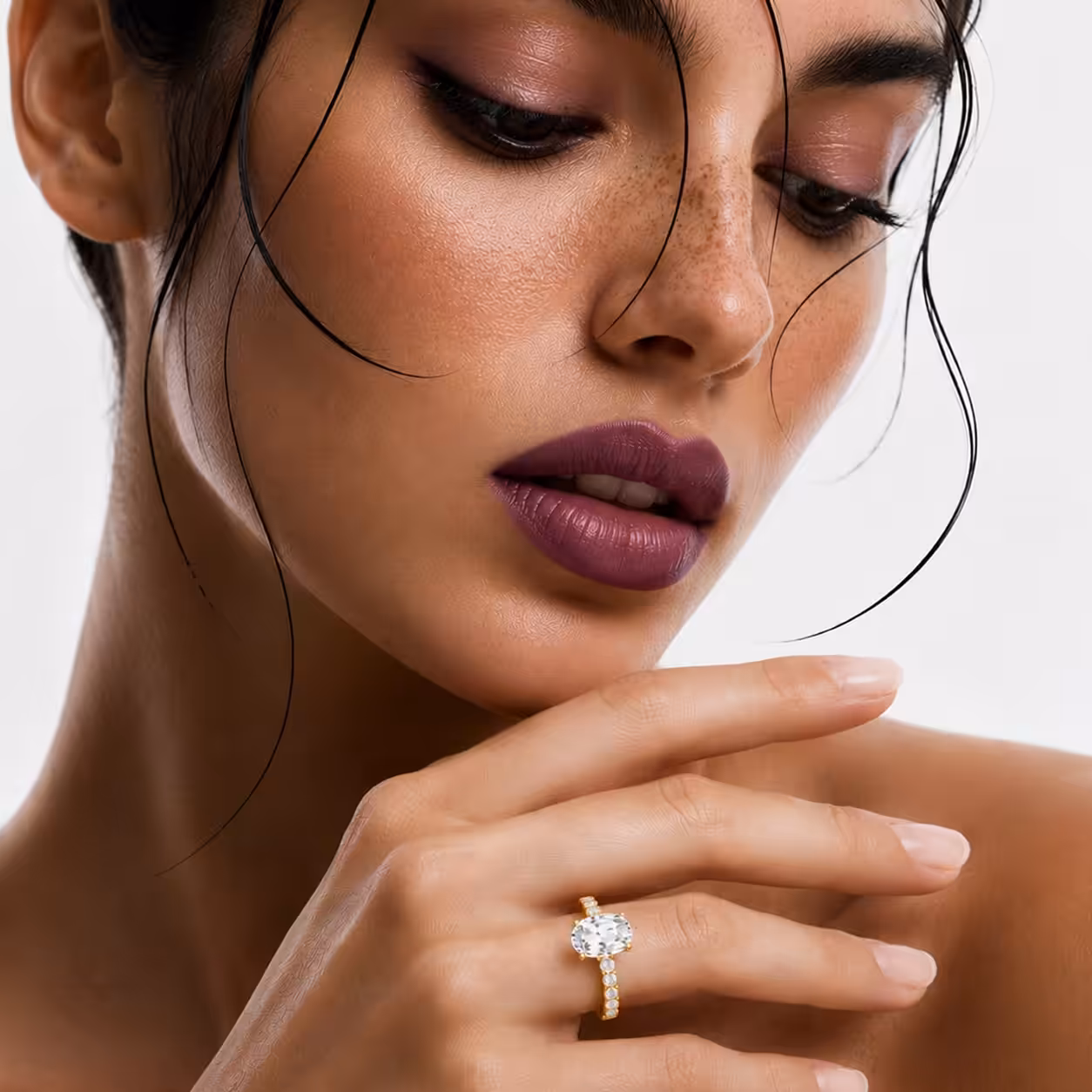 Close-up of a model with dark hair and rich plum lipstick wearing a pavé set lab-grown oval shaped diamond engagement ring.