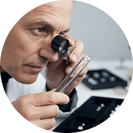 A circular photograph of a focused gemologist using a jeweler's loupe and tweezers to closely inspect a loose La Joya lab-grown diamond, representing expert curation and hand-selected stones backed by over 35 years of professional industry experience.
