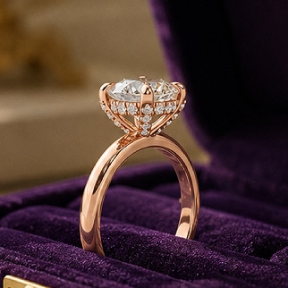 Finished rose gold engagement ring with a large radiant-cut center diamond resting in front of an open purple velvet ring box.