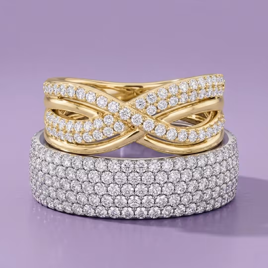 A thick white gold multi-row lab-grown diamond pavé band stacked below a yellow gold infinity-style diamond fashion ring on a purple background.