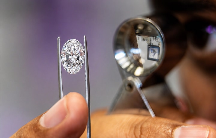 Close-up of a jeweler using tweezers and a magnifying jeweler's loupe to inspect a clear oval-cut diamond.