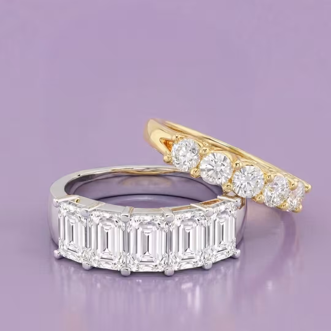 A white gold five-stone emerald-cut lab-grown diamond ring displayed next to a yellow gold five-stone round-cut lab-grown diamond ring on a purple background.