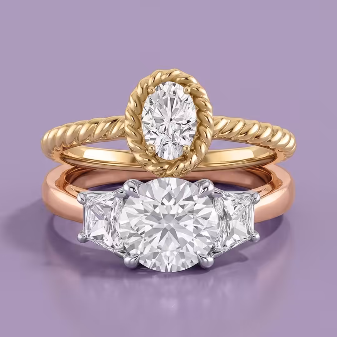 A rose gold three-stone round lab-grown diamond engagement ring stacked with a yellow gold oval-cut lab-grown solitaire diamond engagement ring on a purple background.