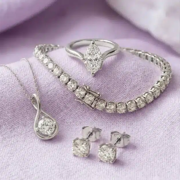 Fine diamond anniversary gift set including a marquise solitaire ring, tennis bracelet, round pendant necklace, and stud earrings on soft lilac fabric