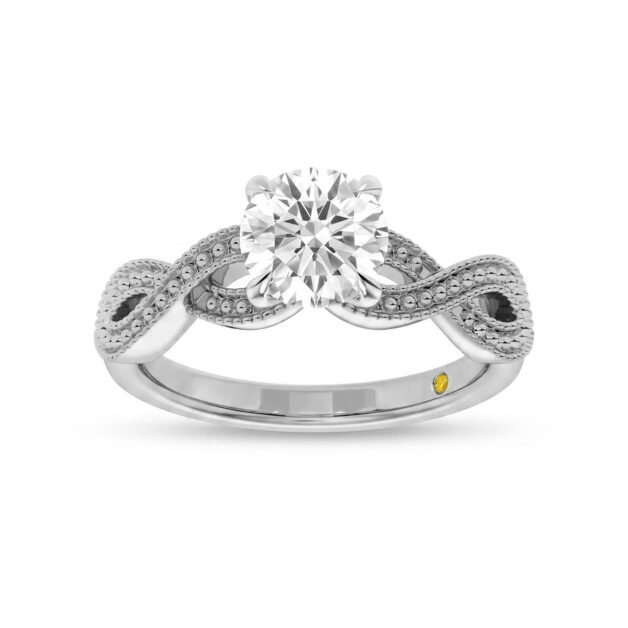 A top-down view of a white gold engagement ring featuring a prominent round shape lab-grown diamond center stone. The band is designed with a detailed, milgrain-edged infinity twist shank and also includes a small signature yellow gemstone set into the inner band. The ring is displayed against a clean white background with a subtle reflection.